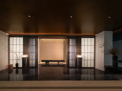 Warm and inviting living room with a wooden floor, a large wooden door, and a central bench, surrounded by a brown color scheme and a potted plant