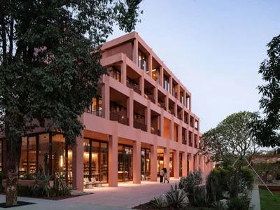 A modern hotel building with a pink and brown color scheme, featuring a courtyard and patio area, with natural light and inviting atmosphere