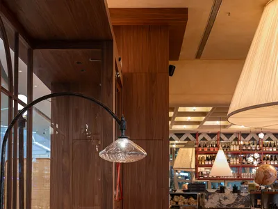 A well-lit restaurant interior with wooden furniture, tables, chairs, and a bar, featuring a modern and contemporary atmosphere