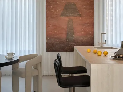 A modern kitchen and dining area with a marble countertop, white walls, a black chair, and a large painting on the wall, set in a warm and inviting dimly lit space