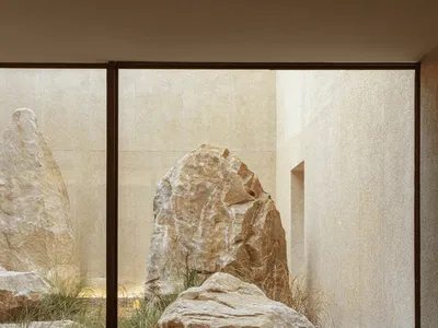 Cozy modern living room with a large rock in the center, a couch on the right, and a chair on the left, surrounded by natural light and modern decor