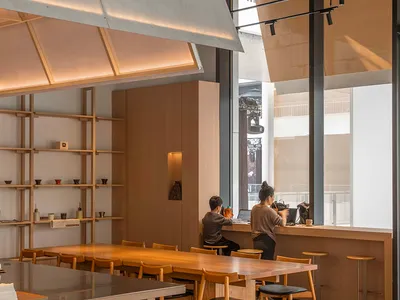A modern restaurant interior with a dining table, chairs, counter, and kitchen elements, featuring wooden accents and a neutral color palette, with soft and warm lighting