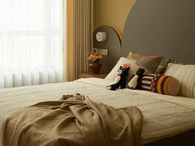 Cozy bedroom with a bed, mirror, and window, featuring a yellow wall, a blanket, pillows, and stuffed animals