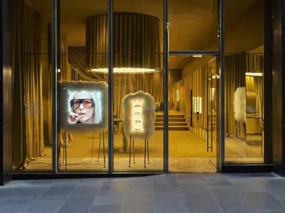 A clothing store display window featuring a mannequin in sunglasses in front of a TV screen, set in a well-lit storefront