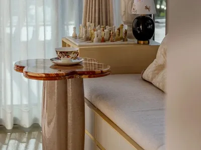 A well-lit living room with a white couch, white curtains, and a vase with flowers on a coffee table