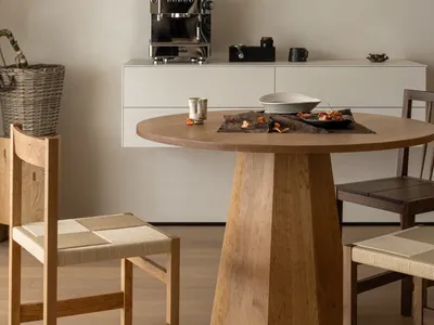A modern kitchen with a wooden dining table and chairs, a refrigerator, microwave, and potted plant, lit dimly for a cozy atmosphere