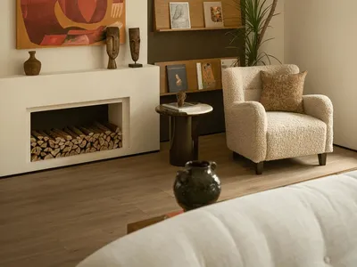 Cozy living room with a fireplace, wooden floor, and a bookshelf filled with books, furnished with a couch and a chair, and well-lit