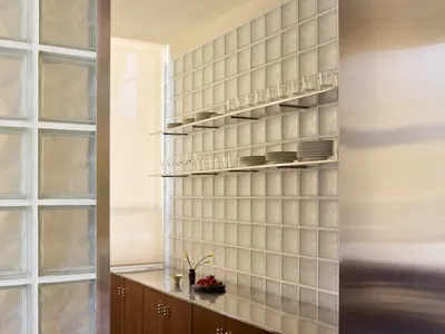 A modern kitchen with a wooden cabinet and glass door, featuring a vase with flowers and wine glasses on the counter, in a well-lit space with a warm atmosphere