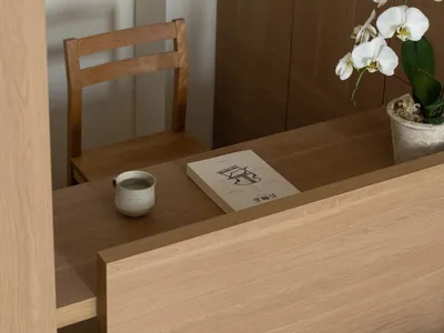 一個充滿著自然光線的舒適家裡工作室，裡面有木製的桌子、椅子和花瓶，裡面插著花