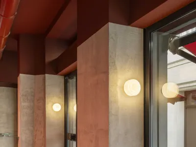 A modern restaurant interior with a row of wooden tables and metal chairs, illuminated by natural light through windows, creating a warm and inviting atmosphere