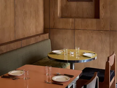 A modern dining room with a wooden table and chairs, set with plates, glasses, and utensils, surrounded by wooden walls and soft, diffused lighting