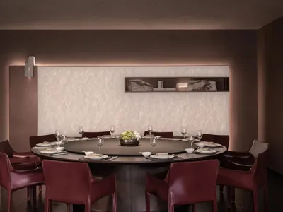 Dining room with a round table set with wine glasses, bowls, and vases, surrounded by chairs, and a couch in the background, featuring wood and marble materials