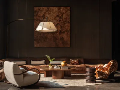 Comfortable living space with a brown couch, chair, and lamp, decorated with a vase, bowl, and book, in a modern and contemporary style with a warm and cozy atmosphere