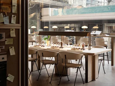 A modern restaurant interior with a large dining table, wooden chairs, and natural light from windows