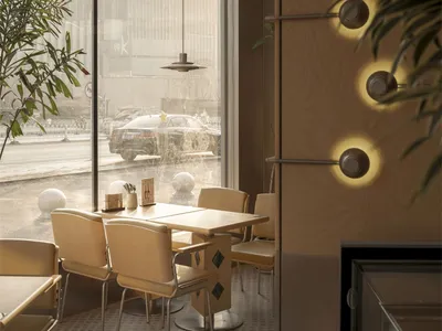 A modern restaurant with a large dining table surrounded by chairs, a potted plant, and a large window, creating a cozy atmosphere with dim lighting