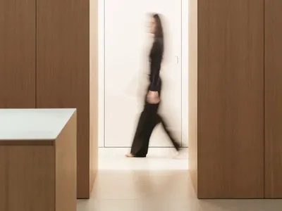 一名穿著黑色禮服的女性走向一間廚房，木地板和白色門