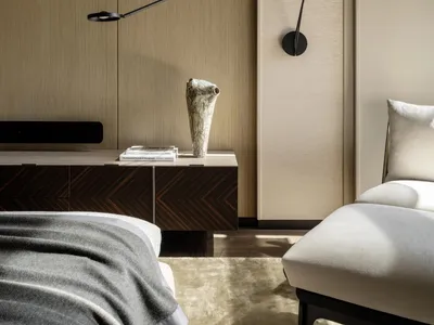 Cozy bedroom with a bed, dresser, and lamp, featuring a wooden floor and tan color scheme, with natural light from a window