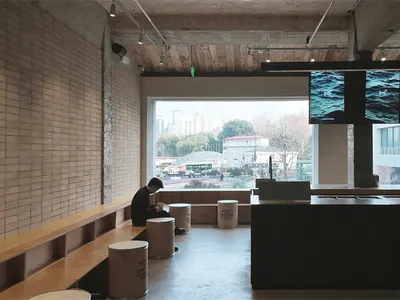 A dark and moody restaurant living space with a bar, dining table, and TVs, featuring a man sitting on a bench