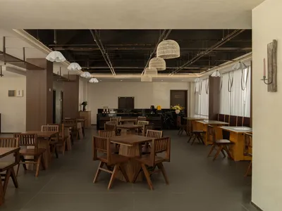 A modern restaurant with a large dining area featuring wooden tables and chairs, well-lit to create a warm and inviting atmosphere