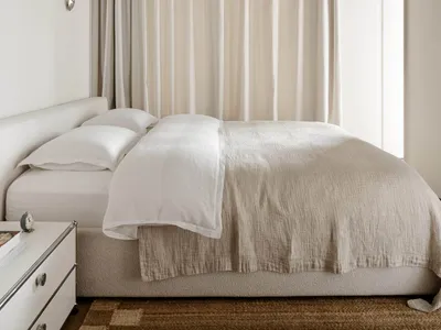 A calm bedroom with a white bed, nightstand, and curtains, lit by natural light from the window