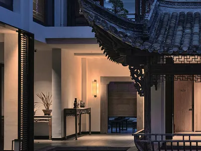 一間充滿光線的房間，類似中國式屋頂，內有游泳池、餐桌和長凳，裝飾著植物、花瓶和碗，使用溫暖的木頭和石頭材料