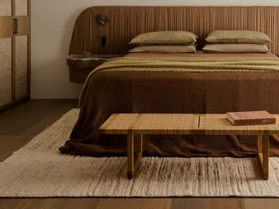Cozy bedroom with a brown bed, table, and chair, surrounded by warm wood tones and natural light