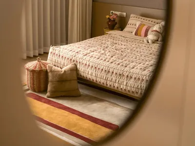 Cozy bedroom with a white comforter and brown blanket, a mirror above the bed, and a rug on the floor