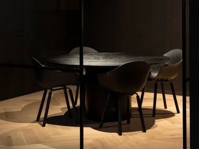 Dimly lit dining area with a black glass-topped table surrounded by wooden chairs, creating a cozy atmosphere