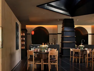 A modern restaurant with a wooden dining table and chairs, set with various items, surrounded by natural light from the windows