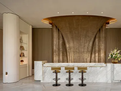 Modern hotel lobby with a marble countertop, curved wall, and soft lighting, featuring a row of stools and a vase with flowers