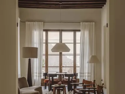 A well-lit living room with a couch, chair, dining table, and multiple chairs, decorated with a rug and lamp, creating a warm and inviting atmosphere