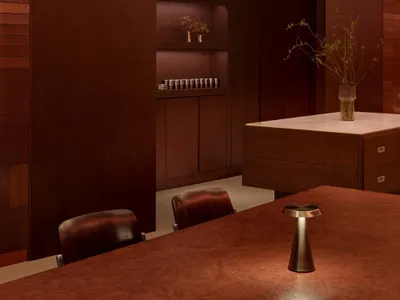 A warm and inviting living space with wooden walls and floor, featuring a wooden table, chair, cabinet, and potted plant