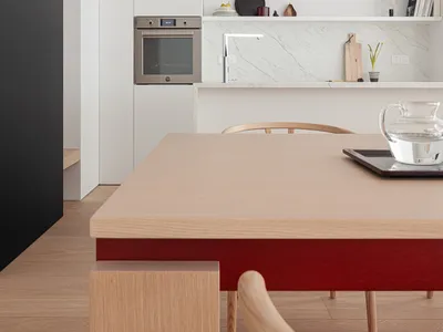 Modern kitchen with a wooden table and chairs, featuring a stove, oven, sink, and refrigerator, with natural light and a vase on the table