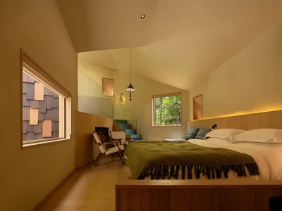 A well-lit bedroom with a wooden floor, a bed, a chair, and a window, creating a comfortable atmosphere