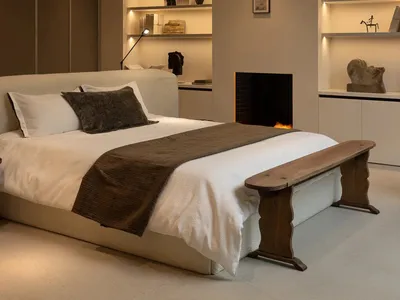 Cozy bedroom with a wooden headboard, brown blanket, and a fireplace, lit by natural light from a skylight