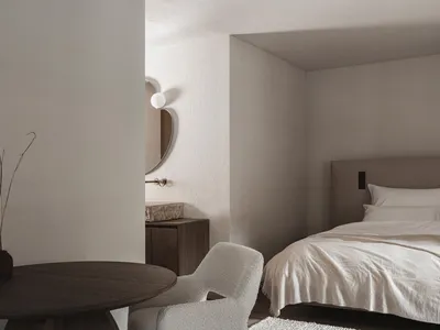 Cozy bedroom with a bed, chair, and table, featuring white furniture and soft warm lighting