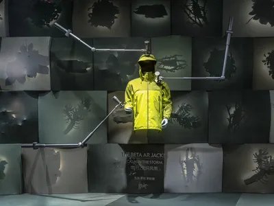 A mannequin in a yellow jacket is displayed in a retail store with a wall of images and items on display