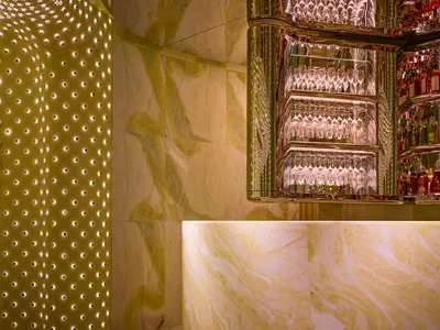 A modern bar with a marble countertop, mirrored surface, and wine glasses, surrounded by bottles and creating a sophisticated atmosphere