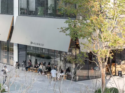 A casual city restaurant with wooden furniture, people seated at tables, and natural sunlight illuminating the scene