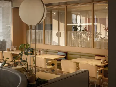 A modern restaurant with a large dining area featuring multiple tables, chairs, and potted plants, with a warm and inviting atmosphere and a combination of wood and metal materials