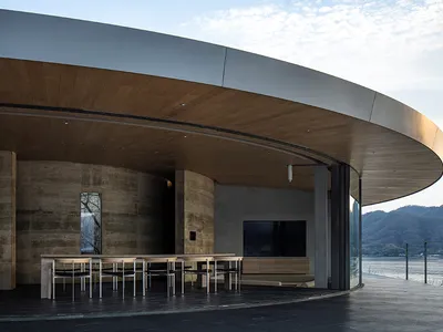 A modern restaurant with a circular seating area featuring a large TV, chairs, and dining tables, surrounded by contemporary materials and well-designed lighting