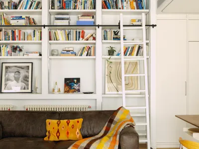 Cozy modern living space with a couch, chair, dining table, and bookshelf, decorated with books and featuring a modern and comfortable style