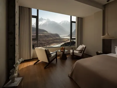 Cozy living room with a large window offering a mountain view, featuring a bed, chair, and dining table, with natural light creating a warm atmosphere
