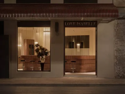 A storefront with a sign reading Love Isabelle, featuring a display of potted plants and chairs in front of a large window, with a warm and inviting atmosphere