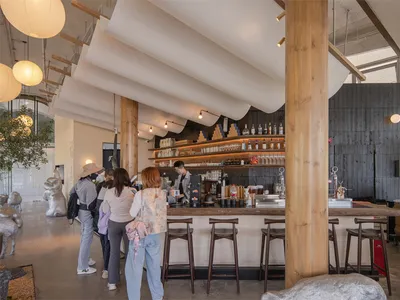 一間木質擺設的餐廳，餐廳內有木制吧台和座位區，配有 stools、吧台、餐桌和椅子，還有多個裝飾品，營造出溫馨的氣氛
