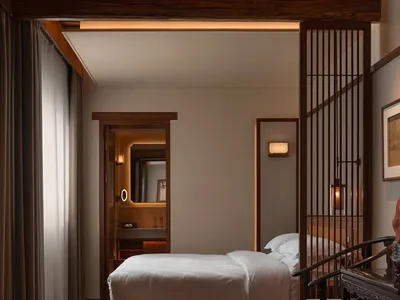 A hotel bedroom with a bed, chair, and desk, featuring wooden furniture and dim lighting, creating a cozy atmosphere