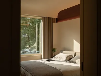 A well-lit bedroom with a bed, window, and curtain, featuring a white comforter and two pillows