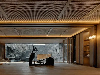 A dimly lit living space with a modern style, featuring a large sculpture on a bench, a dining table, and chairs, with a combination of wood and metal elements