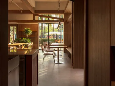 Cozy modern restaurant interior with a wooden dining table and chairs, dim lighting, and a visible kitchen counter in the background