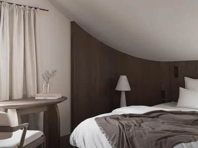 Cozy bedroom with a wooden bed frame, a wooden floor, and a dimly lit atmosphere, featuring a bed, a table, and a lamp